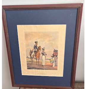 Peut inclure: Estampe ancienne encadrée représentant des soldats en uniformes colorés, dont un à cheval, un tambour et d'autres personnages. L'estampe est encadrée sur fond bleu dans un cadre en bois foncé, illustrant l'habillement militaire historique.