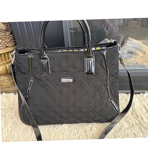 May include: Black quilted tote bag with patent leather accents. The bag features a diamond pattern, a top handle, and a detachable shoulder strap. A small silver-tone plaque is centered on the front of the bag.