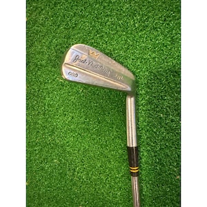 Puede incluir: Un hierro de palo de golf Jack Nicklaus vintage. La cabeza del palo es plateada con el nombre "Jack Nicklaus" y un logotipo de corona. El eje es plateado con detalles en negro y amarillo. El palo está sobre un fondo verde.