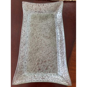 Puede incluir: Bandeja rectangular de vidrio con una superficie texturizada y moteada. La bandeja tiene lados suavemente curvados y una apariencia clara y esmerilada. Ideal para servir aperitivos o exhibir objetos decorativos.