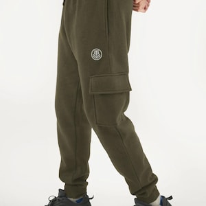 Puede incluir: Pantalones de chándal cargo verde oliva con cintura con cordón y un pequeño logotipo en la parte superior izquierda de la pierna. Los pantalones tienen un bolsillo cargo en la pierna derecha y zapatillas negras.