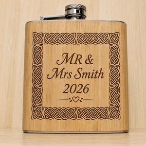 May include: A rectangular bamboo flask with a silver metal screw cap. The front features a dark engraved Celtic knot border surrounding the text "MR & Mrs Smith 2026" and a small heart symbol centred below the year in a clean, legible font.