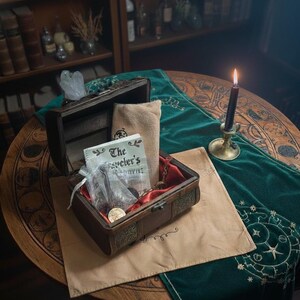 May include: A wooden treasure chest with ornate metal detailing, open to reveal a red-lined interior and various items. A small bag, a book titled "The Traveler's", and other trinkets are inside. The chest sits on a tan cloth, with a green velvet runner and a lit candle nearby.
