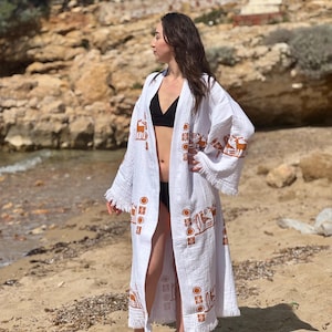 May include: White long-sleeved robe with a brown geometric pattern and fringe trim. The robe is open in the front and has a V-neckline.