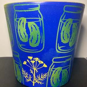May include: A blue ceramic planter with a green and yellow design of dill and jars of pickles.
