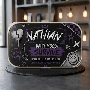 May include: A rectangular lunch box with a black and purple graphic design featuring the name NATHAN, the text DAILY MOOD: SURVIVE, FUELED BY CAFFEINE, and GOOD FOOD GOOD VIBES, alongside illustrations of a broken heart, skull, and smiley face.