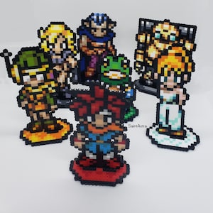 May include: A set of 8-bit pixel art characters made with perler beads. The characters include a warrior, a mage, a frog, a knight, a princess, and a robot. The characters are all standing on small bases.