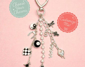 May include: A silver-toned 3-strand purse charm featuring a heart-shaped clasp and various dangling charms including a yin-yang, horseshoe, 8-ball, checkered heart, star, pearl strand, letter S, dragonfly, cross, MAMA text, and clover.