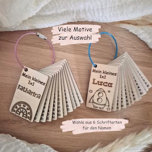 May include: Two sets of rectangular wooden cards on metal rings. The left set features a rainbow design and the name Katharina, with text reading Mein kleines 1x1. The right set features a rocket design and the name Luca, with text reading Mein kleines 1x1.