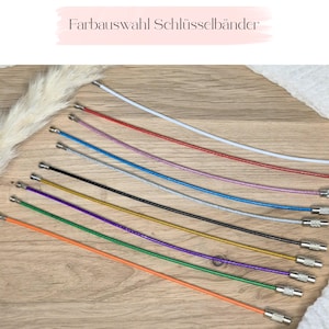 May include: A collection of ten flexible wire key rings in various colors including white, red, pink, blue, silver, black, gold, purple, green, and orange. Each ring features a threaded metal screw closure at the ends for securing keys.