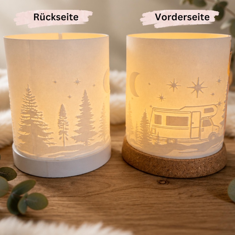 May include: Two cylindrical paper lanterns illuminated from within. The left lantern, labelled R&uuml;ckseite, features a forest silhouette with stars and a crescent moon. The right lantern, labelled Vorderseite, shows a camper van, stars, and a moon.