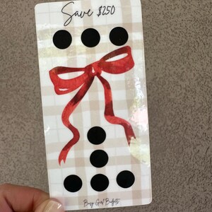 May include: A rectangular card with a plaid pattern, featuring a red bow and black dots. The text "Save $250" is at the top. The words "Busy Girl Budgets" are at the bottom.