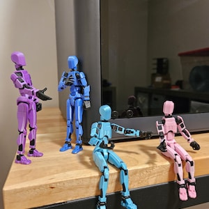 May include: Four articulated action figures in different poses. The figures are made of plastic and are painted in various colours, including purple, blue, light blue, and pink.