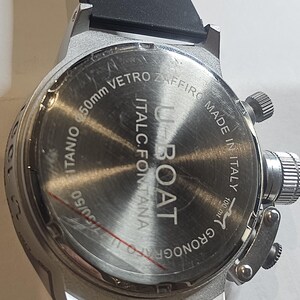 May include: A silver-toned U-Boat watch with a black rubber strap. The watch face features the text "U-BOAT" and "MADE IN ITALY". The watch is 50mm in diameter.