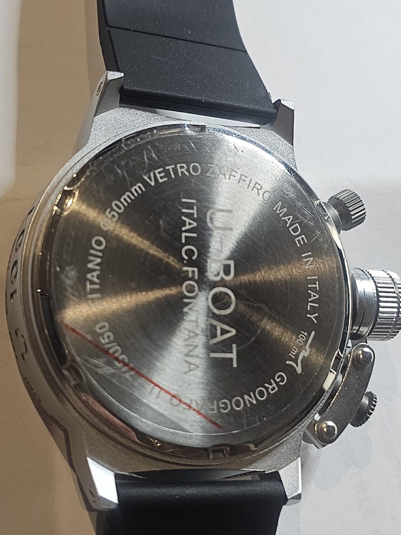 May include: A silver-toned U-Boat watch with a black rubber strap. The watch face features the text "U-BOAT" and "MADE IN ITALY". The watch is 50mm in diameter.