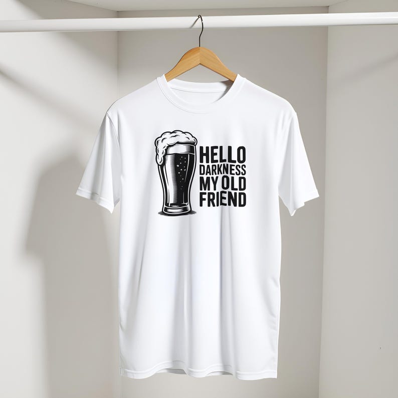 May include: White t-shirt with a black and white graphic of a beer glass and the text "HELLO DARKNESS MY OLD FRIEND". The beer glass has a foamy head. The shirt is hanging on a wooden hanger.