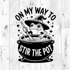 May include: Black and white graphic featuring a frog wearing a witch hat, stirring a cauldron. The text reads "ON MY WAY TO STIR THE POT". Stars and other decorative elements surround the frog and cauldron.
