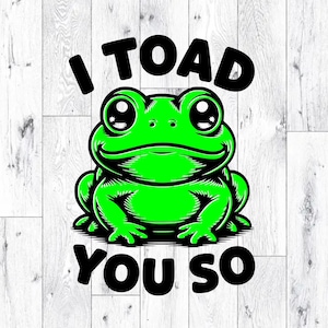 May include: A cartoon frog in bright green with black outlines and the text "I TOAD YOU SO". The frog has large eyes and a smiling expression. The text is in bold black letters. The background is a white wood grain pattern.