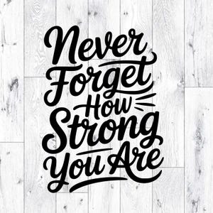 Puede incluir: Texto negro sobre fondo de madera blanca: "Never Forget How Strong You Are". Las palabras están escritas en cursiva, con "How" en un tamaño de fuente más pequeño. Para decoración.