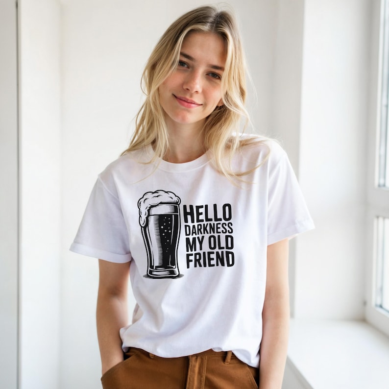 May include: White t-shirt with the phrase "HELLO DARKNESS MY OLD FRIEND" and a black and white illustration of a beer glass. The shirt is short-sleeved and made of a soft material.