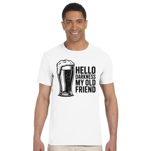 May include: White t-shirt with a black and white graphic of a beer glass and the text "HELLO DARKNESS MY OLD FRIEND". The shirt is a crew neck style.
