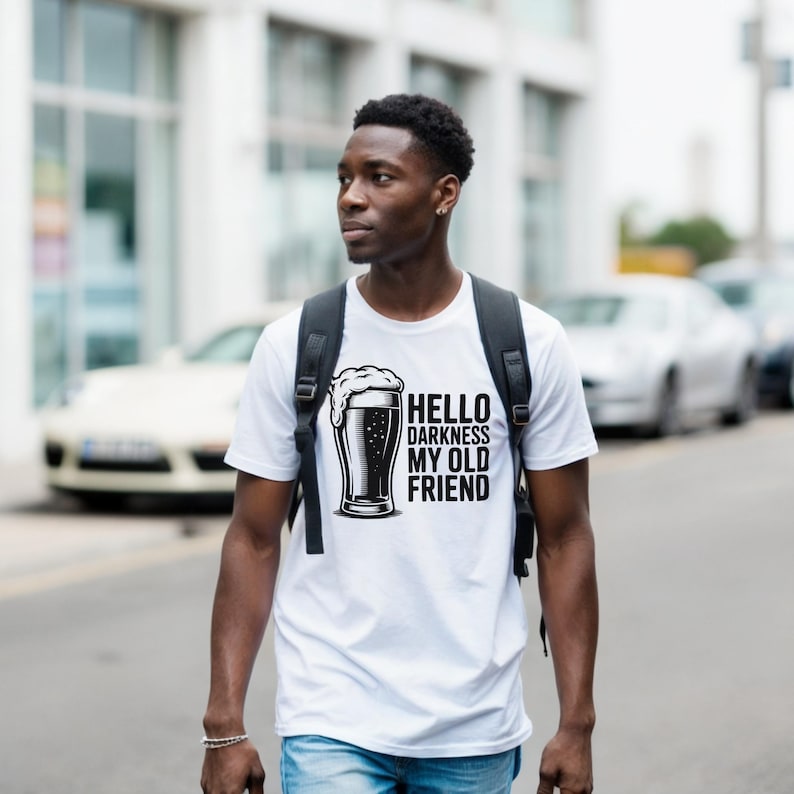 May include: White t-shirt with a black graphic of a beer glass and the text "Hello Darkness My Old Friend." The shirt is short-sleeved and worn by a person with a backpack.