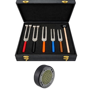 May include: A set of five metal tuning forks with colored handles in red, black, orange, blue, and brown, stored in a black case with a wooden mallet. A black circular tuning fork activator with a geometric pattern and text reading TUNING FORK ACTIVATOR.