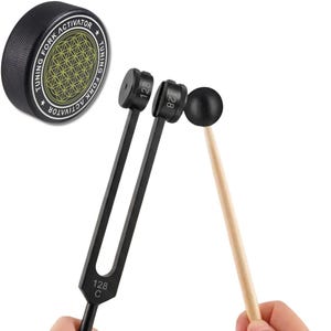 Könnte beinhalten: Eine schwarze Stimmgabel mit der Aufschrift 128 C, ein schwarzer Gummihammer mit Holzgriff und ein runder, schwarzer Stimmgabel-Aktivator-Puck mit goldenem Blume-des-Lebens-Muster und dem in Weiß gedruckten Text TUNING FORK ACTIVATOR.