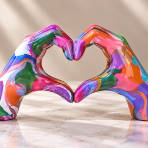 May include: A decorative sculpture featuring two hands joined together to form a heart shape. The surface is finished with a vibrant, multi-colored marbled pattern including shades of bright pink, orange, purple, green, and white swirls.
