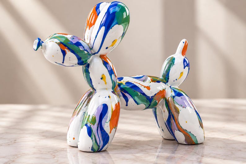 May include: A glossy white balloon dog sculpture featuring a vibrant multi-colored paint drip pattern in shades of blue, green, orange, and purple. The figurine is shaped like a twisted balloon animal with a rounded head, body, and four legs.