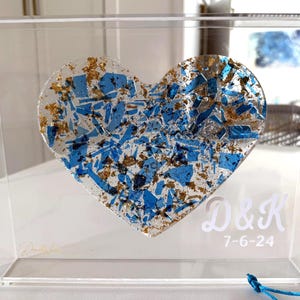 May include: A clear acrylic box frame containing a heart-shaped resin piece filled with blue glass shards and gold leaf flakes. The front of the frame features the white printed text D&K and the date 7-6-24, with a small blue tassel attached.