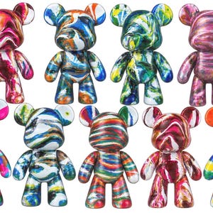 May include: A collection of nine bear-shaped figurines featuring various marbled and swirled paint patterns in vibrant colors including pink, blue, green, orange, and yellow. Each figure has rounded ears, a smooth surface, and a standing pose.