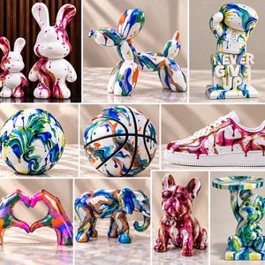 May include: A collection of decorative sculptures and objects featuring white surfaces with vibrant, multi-colored paint drip patterns. Items include rabbit figures, a balloon dog, a boxing glove with the text NEVER GIVE UP, a soccer ball, a basketball, a sneaker, heart-shaped hands, an elephant, a French bulldog, and a bear holding a tray.