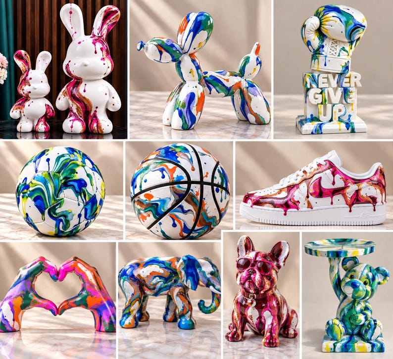May include: A collection of decorative sculptures and objects featuring white surfaces with vibrant, multi-colored paint drip patterns. Items include rabbit figures, a balloon dog, a boxing glove with the text NEVER GIVE UP, a soccer ball, a basketball, a sneaker, heart-shaped hands, an elephant, a French bulldog, and a bear holding a tray.