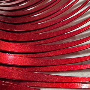 May include: Close-up of a red metallic surface with a glittery finish. The surface is made up of many thin, curved strips of metal.