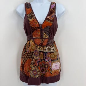 May include: A sleeveless top featuring a deep V-neckline with a row of small buttons. The garment is crafted from solid brown fabric combined with a vibrant, multi-colored paisley and geometric patterned panel in shades of orange, purple, and gold.