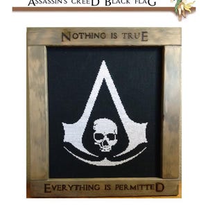 May include: Cross-stitch artwork featuring the Assassin's Creed logo, a white emblem on a black background, framed in wood. The frame includes the phrases "NOTHING IS TRUE" and "EVERYTHING IS PERMITTED". The artwork is a fan-made item.