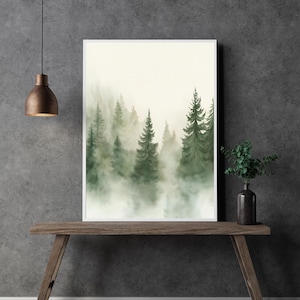 Könnte beinhalten: Ein gerahmter Aquarelldruck einer nebligen Waldszene. Das Kunstwerk zeigt hohe, grüne Nadelbäume, die aus einer Nebelschicht auftauchen. Der Druck wird auf einem Holztisch vor einer grauen Wand mit einer Hängeleuchte präsentiert.