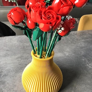 May include: A vibrant bouquet of red roses in a yellow vase. The roses are made of plastic and have green stems. The vase is a bright yellow color and has a ribbed design.