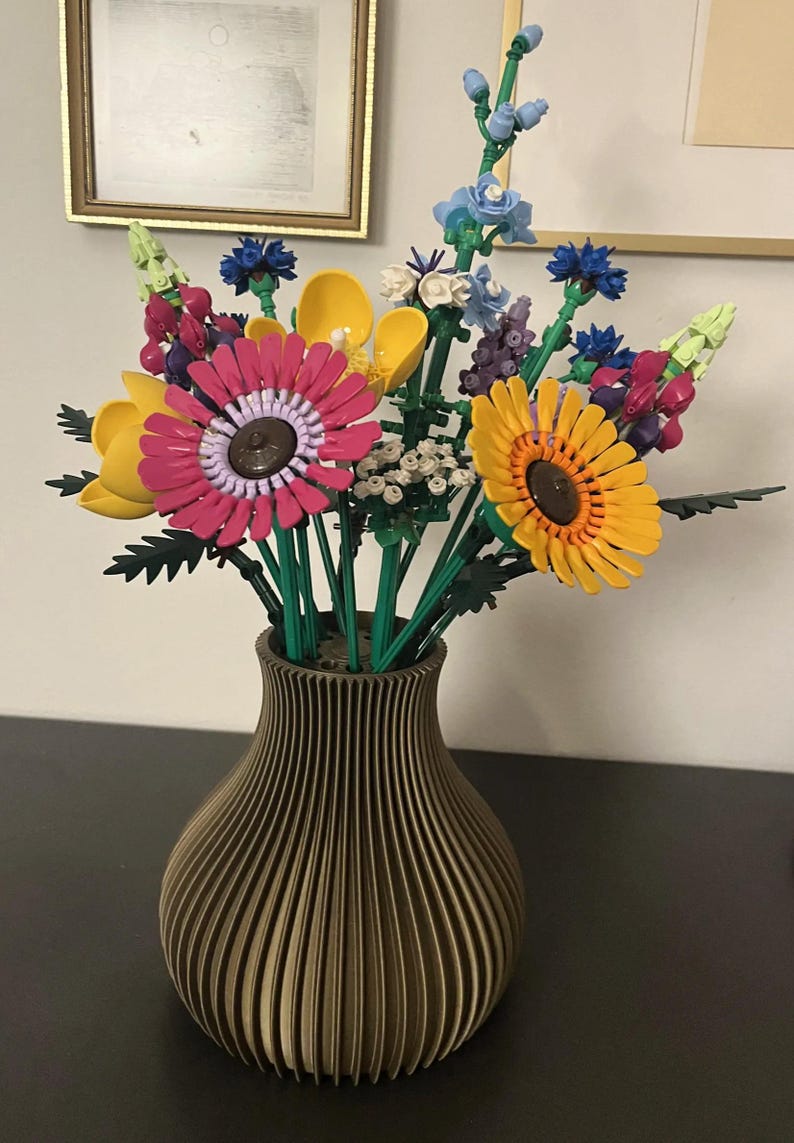 May include: A colorful bouquet of flowers in a brown vase. The flowers include pink, yellow, and blue blooms with green stems. The vase has a ribbed design.