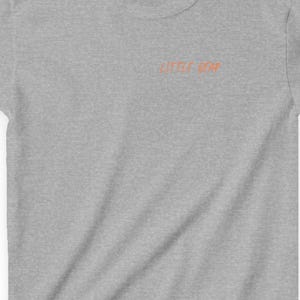 May include: A heather gray t-shirt with the text "LITTLE MAN" in orange lettering across the chest. The shirt has short sleeves and a crew neck. The shirt is made of a soft, comfortable material.