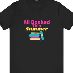 May include: Black t-shirt with the text "All Booked This Summer" in pink and yellow. Below the text is a graphic of a stack of colorful books and a blue bookmark.