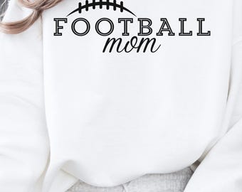 May include: White sweatshirt with the text "FOOTBALL mom" in black, above a football graphic. The sweatshirt is long-sleeved and appears to be made of a soft material. The person is wearing a necklace and sitting down.