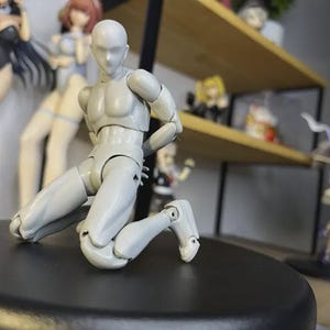 Puede incluir: Una figura articulada gris en posición de rodillas. La figura tiene una forma de cuerpo humano realista y está hecha de plástico.