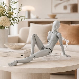 Peut inclure: Une figurine articulée gris clair avec une tête lisse sans traits et une musculature définie. La figurine est dans une position allongée, soutenue par un support et une base en plastique transparent, montrant de multiples articulations.