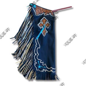 May include: Dark blue leather chaps with a decorative cross and fringe. The chaps feature a brown leather yoke with floral tooling and white and turquoise accents. A leather strap extends from the top.