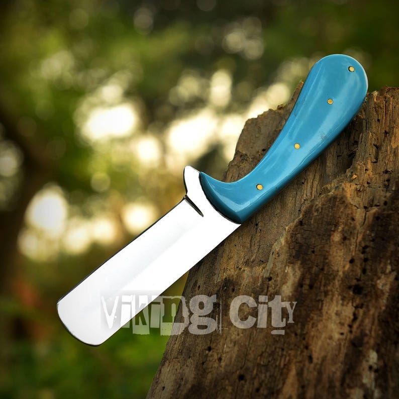May include: A straight razor with a polished steel blade and a curved, light blue handle. The handle has three small, gold-colored rivets. The text "Viking City" is visible on the blade.