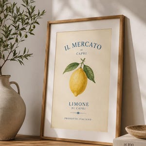 Könnte beinhalten: Ein gerahmtes vertikales Wandbild mit einer gelben Zitrone und grünen Blättern auf cremefarbenem Hintergrund. Der Text lautet IL MERCATO DI CAPRI, LIMONE DI CAPRI und PRODOTTO ITALIANO in blauer Schrift. Der Druck befindet sich in einem hellen Holzrahmen.
