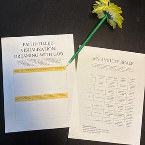 May include: Two printed worksheets with text, "Faith-Filled Visualization: Dreaming with God" and "My Anxiety Scale", are on a dark surface. A yellow flower is attached to a green pencil, resting on the papers. The worksheets have text and tables.