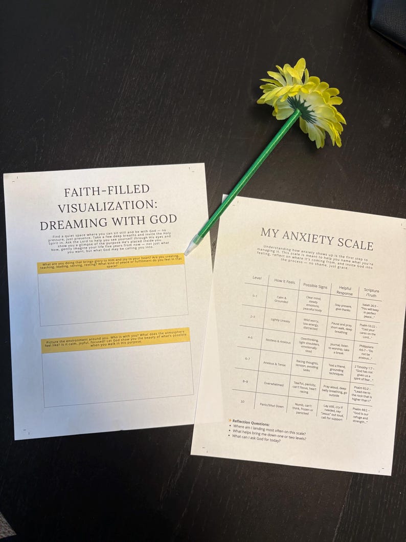 May include: Two printed worksheets with text, "Faith-Filled Visualization: Dreaming with God" and "My Anxiety Scale", are on a dark surface. A yellow flower is attached to a green pencil, resting on the papers. The worksheets have text and tables.